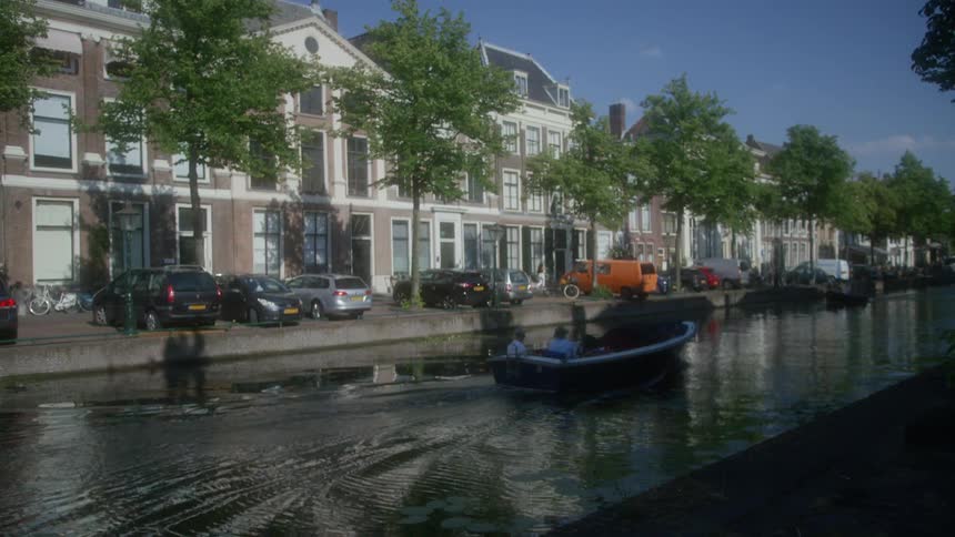 People riding a boat on a canal in the middle of an urban city during the day