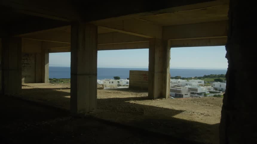 A dark unfinished building with views of a waterfront city through large openings