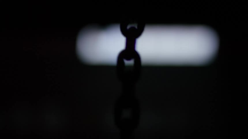 Silhouette of a chain moving up and down inside a dark room