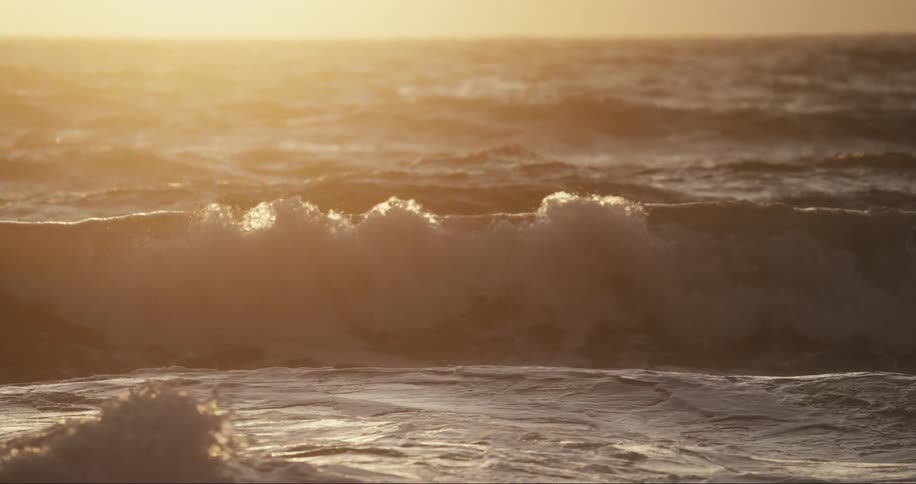 Waves splash as they roll into shore as the sun shines brightly on the horizon