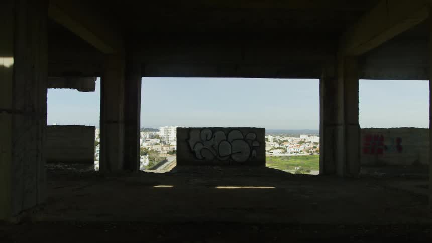 A concrete building with graffiti and open windows showing a cityscape