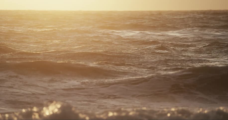 Waves splash as they roll into shore as the sun shines brightly on the horizon