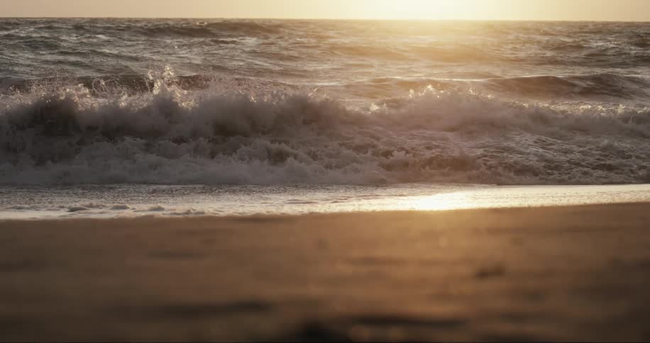 Landscape of sea waves arriving on the beach sand with a sunset on the horizon