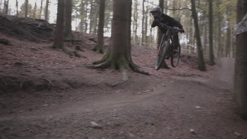 A teenager riding a bike on a trail through the woods leaps into the air