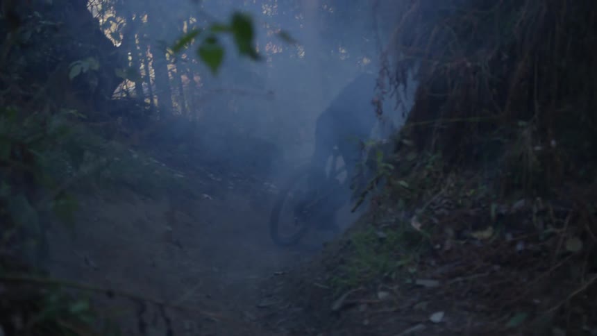 A cyclist rides a mountain bike on a smoke filled trail through the woods