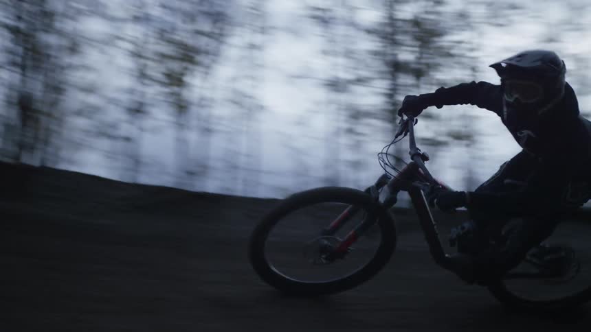A person riding a bike with safety equipment on a dirt track and there are many trees around