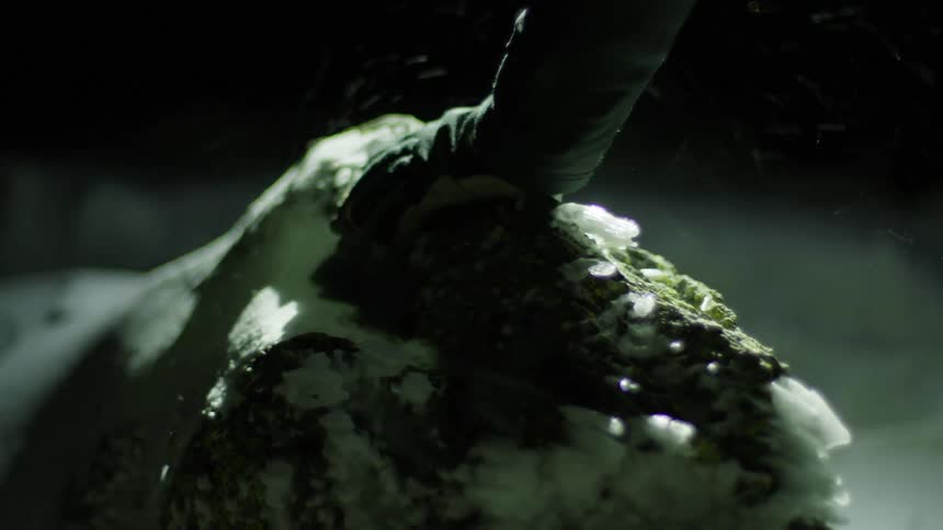 A person hiking through the snow places their hand on a rock for support