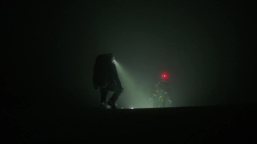 Two people are walking in darkness using a headlamp or a flashlight on a helmet