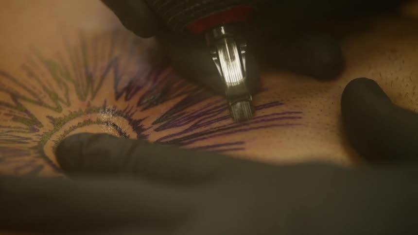 Extreme closeup on the hands of a tattoo artist with gloves and an accessory performing his art on a persons skin