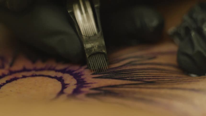 Extreme closeup on the hands of a tattoo artist with gloves performing the tattoo on a persons skin