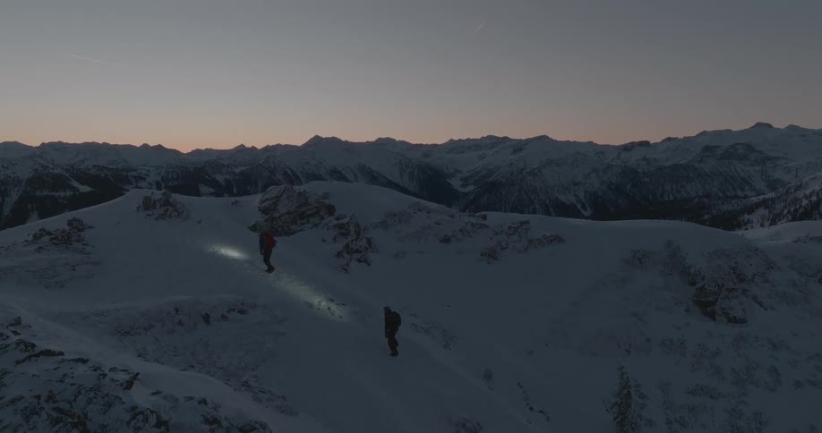 Two people are walking to the peak of a mountain whose ground is covered in snow