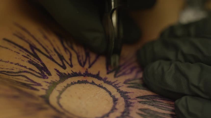 Closeup of the hands of a tattoo artist with gloves performing art on a persons skin
