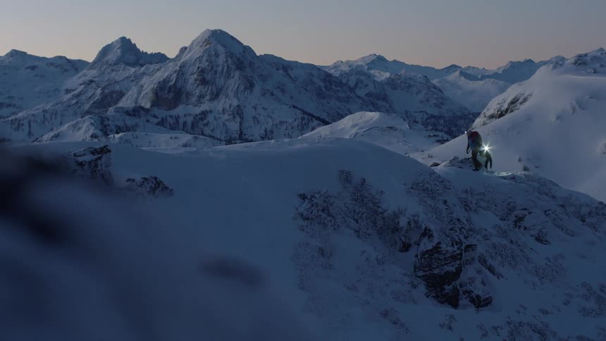 Two people wearing headlamps walk across a snow covered mountain