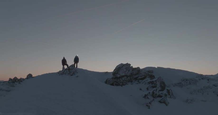 Two people on the peak of a mountain covered by snow in a morning sky