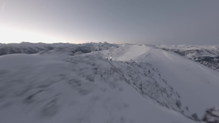 Aerial of people climbing a snow ridge during dusk in winter