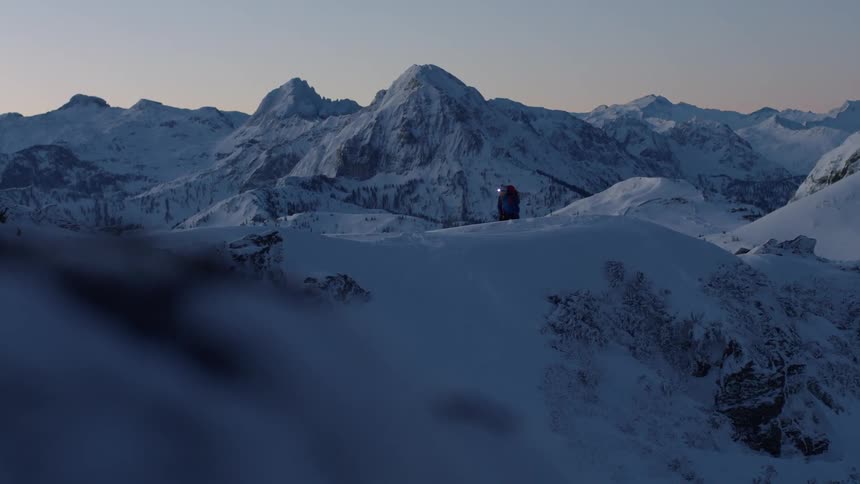 Two mountain climbers wearing headlamps walk across a snow covered mountain