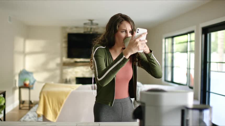 A woman using a smartphone grabs a cup and drinks from it