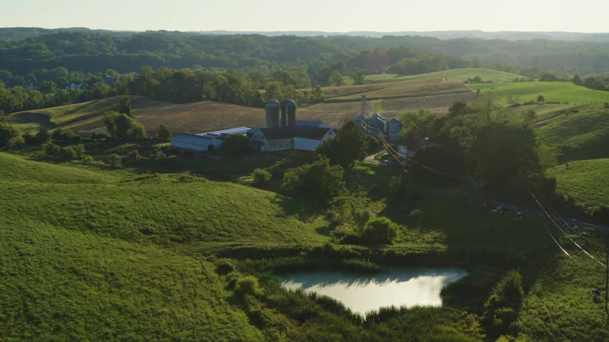 The camera flies above a rural farm surrounded by rolling terrain