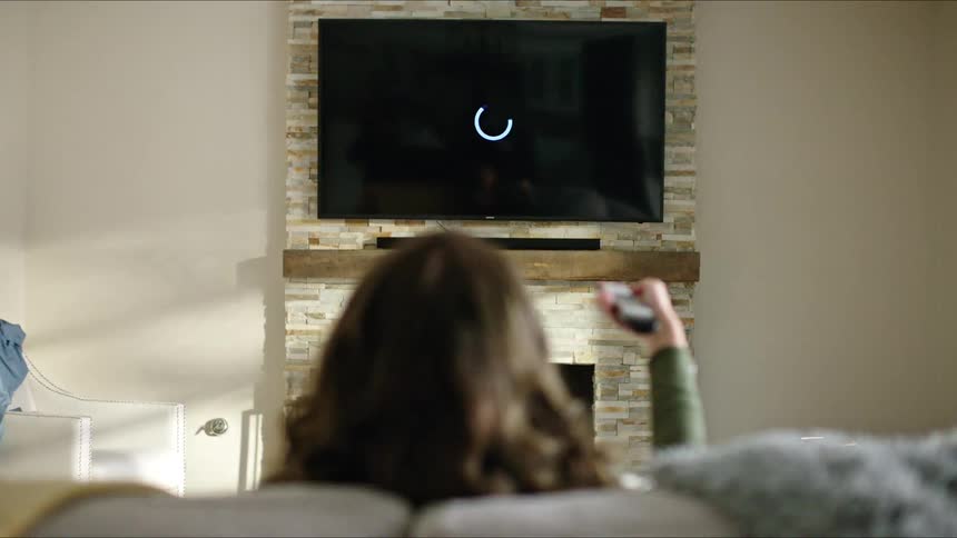 Woman sitting on the couch and pointing the remote at her television