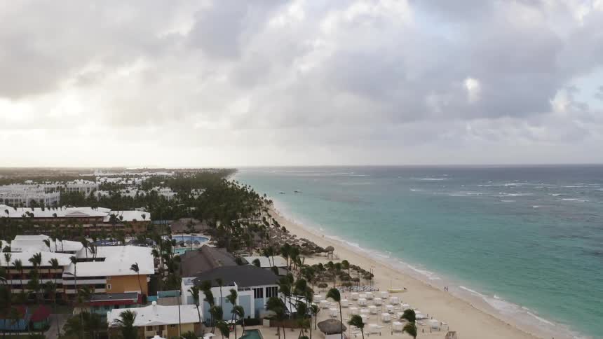 Aerial of a coastal town with paradisiacal beach during a cloudy sunset