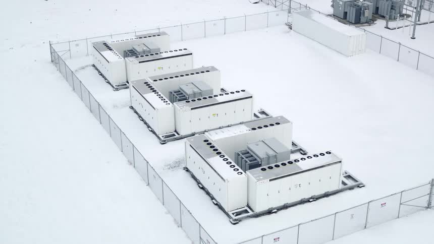 A snowy landscape with several large industrial battery units in a fenced area