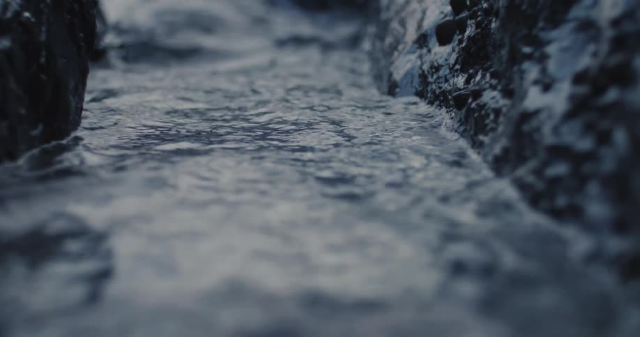 A small flow of water surges along a narrow channel lined by rocks