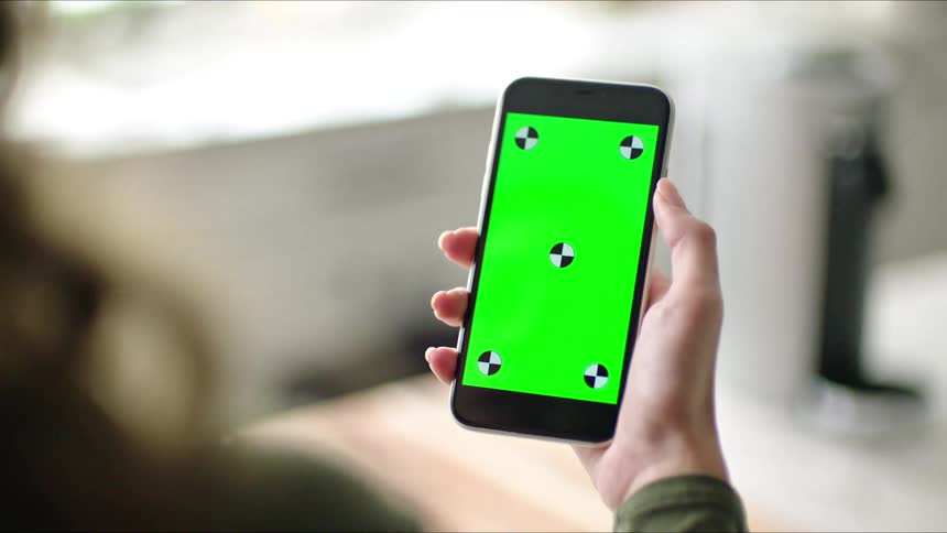 A person holding a cell phone with a green screen