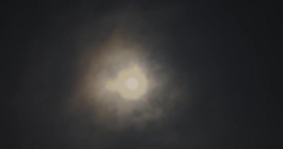 Upward view of the moon illuminating the passing clouds at night