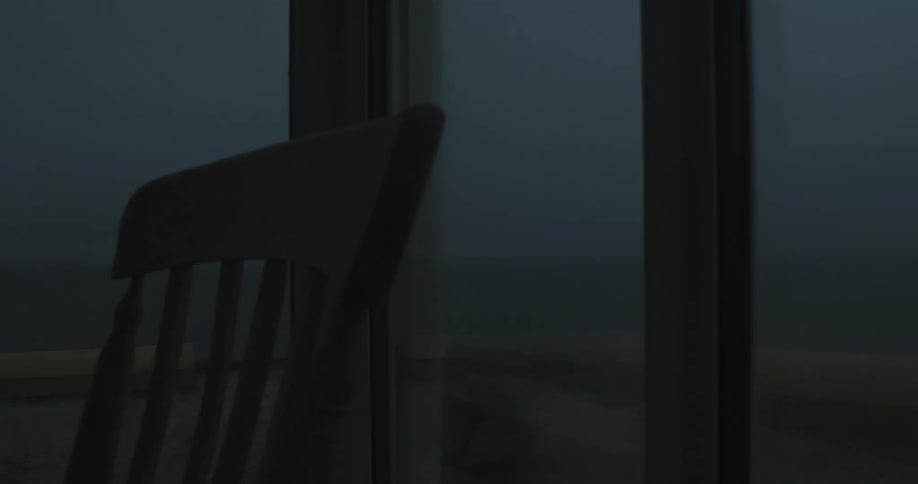 Closeup on a chair inside a mirrored room overlooking a sea on a dark morning