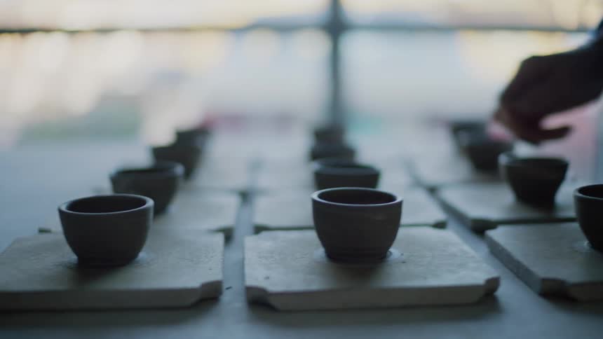 Close in the hands of a woman removing small porcelain cups from a table
