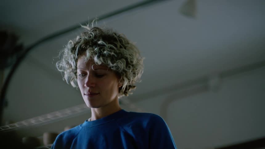 A person standing in a blue shirt is looking down and gives a smile