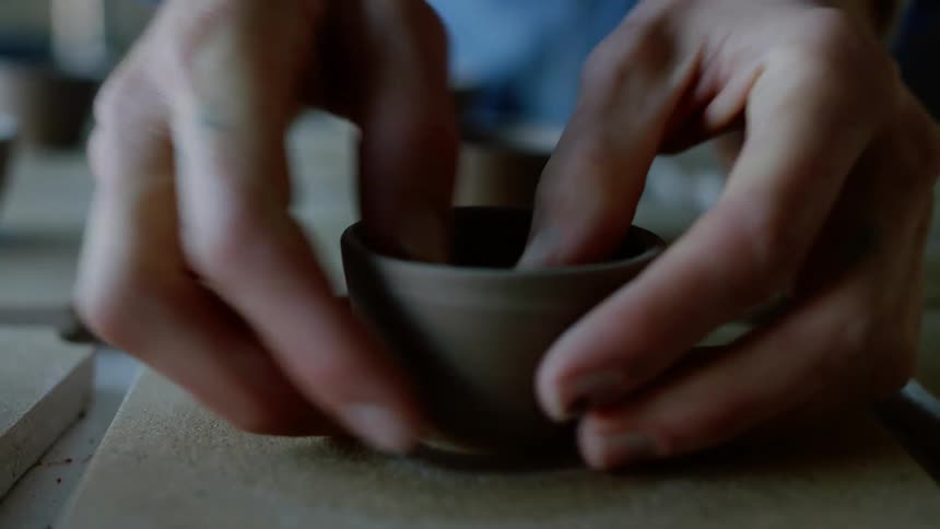 Closeup of a womans hands performing manufacturing work on a small clay cup
