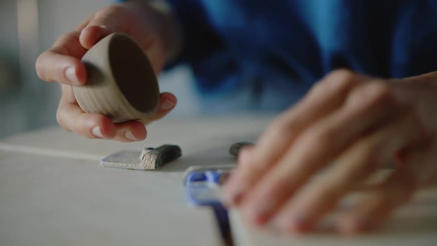 Hands of a woman sculpting a small porcelain cup
