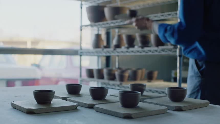A person placing clay cups on a table