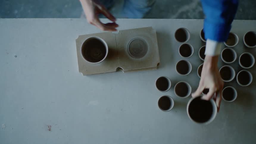 A white woman places pottery cups on a table