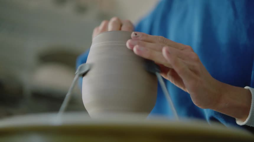 Female potter in workshop shapes pot braced on potters wheel