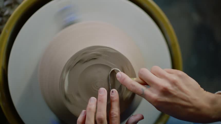 Female potter shapes bottom of pot sitting on turning potters wheel