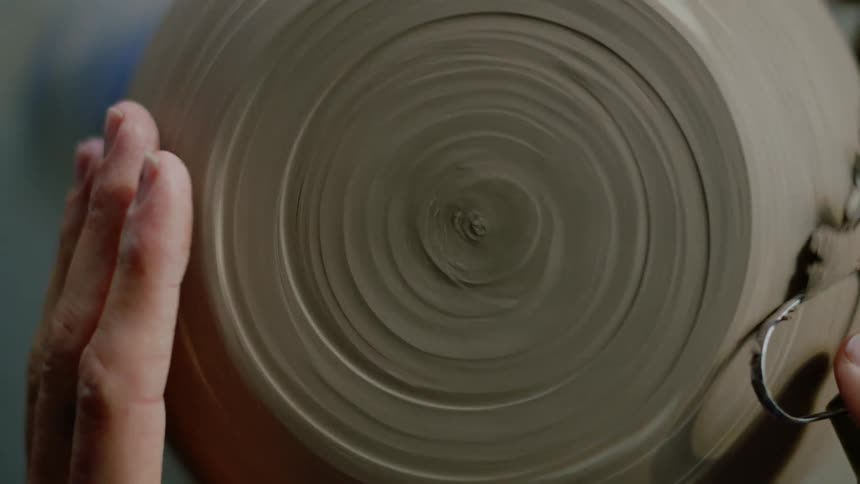Closeup of a womans hands modeling a clay vase with her hands and a small tool