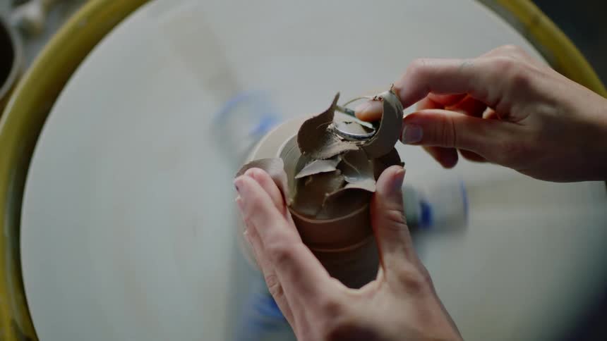 Female potter shapes clay on pottery wheel by shaving it with a tool