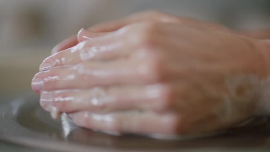 A person modeling a mass of clay on a rotating base