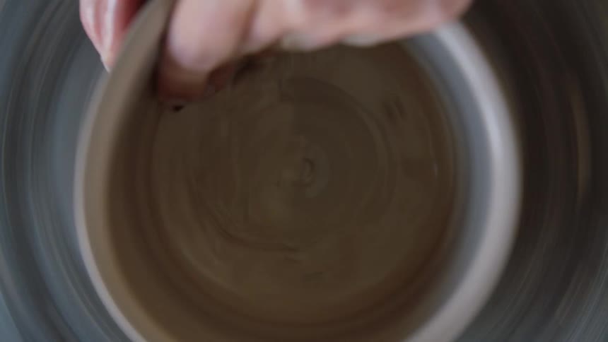 A womans hand modeling clay on a rotating machine