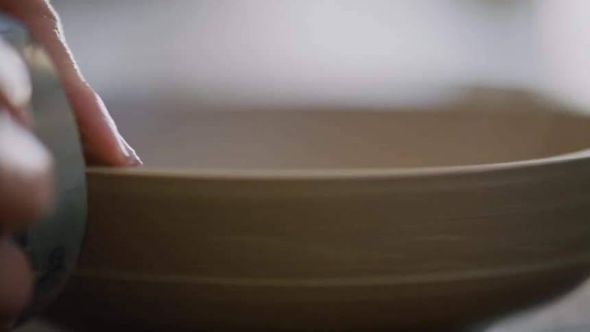 Potter shapes low sided bowl with a metal tool