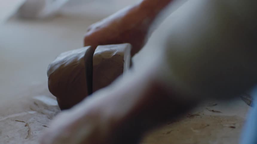 A person cutting a piece of clay with a string