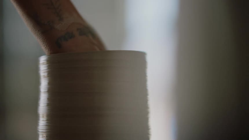 A woman shaves and shapes a piece of clay