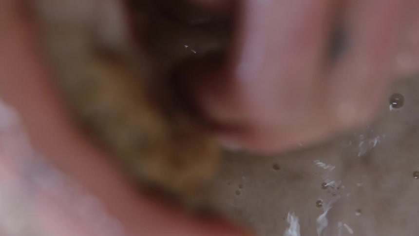A persons hands inside a clay water and squeezing a foam