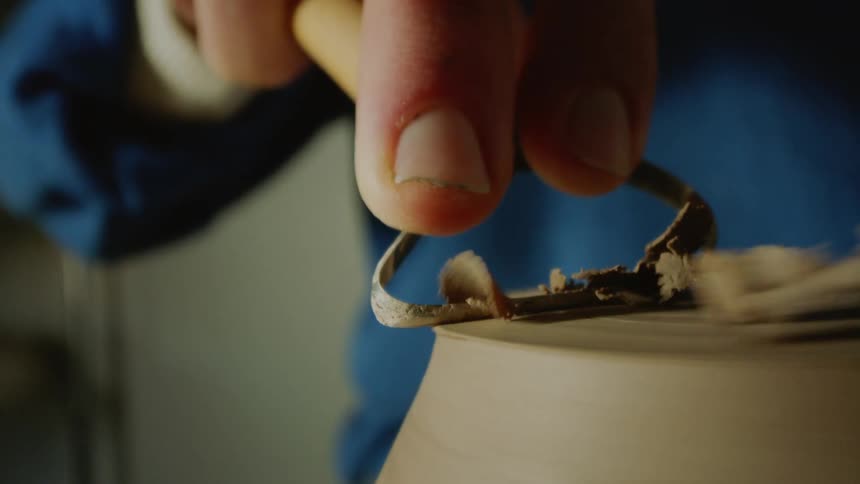 Closeup of a womans hand with a tool sculpting a vase in clay