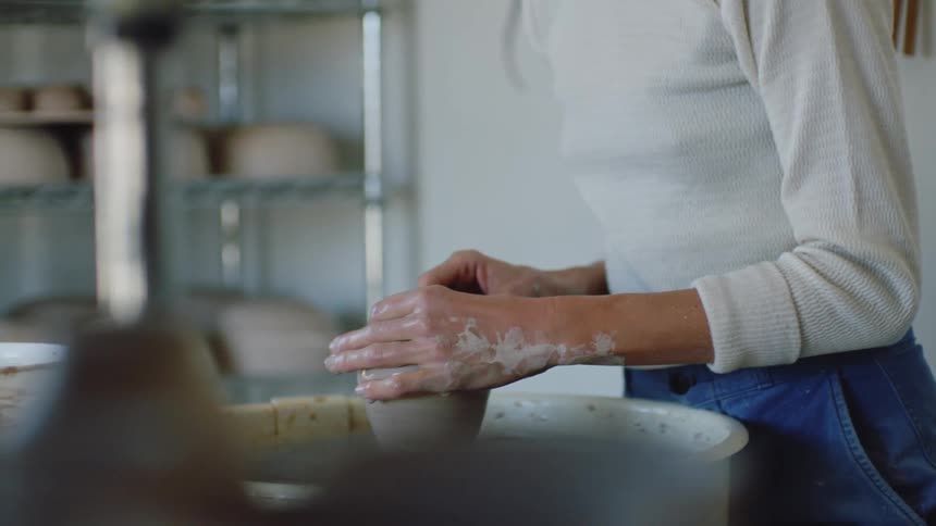 A white woman shapes clay on a pottery wheel