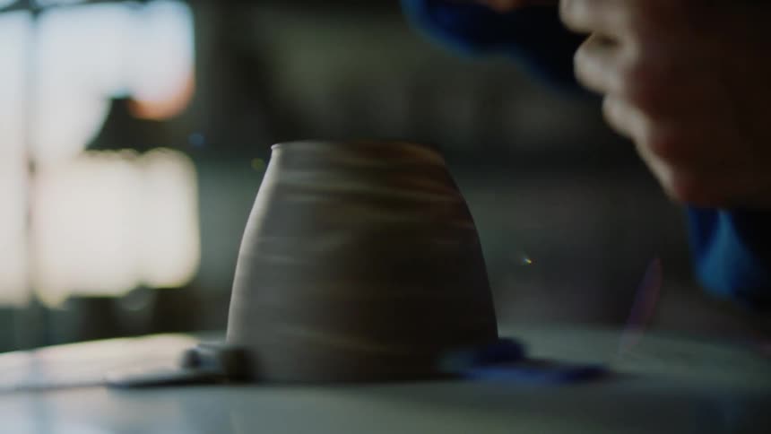 A person shaping a clay cup with a tool
