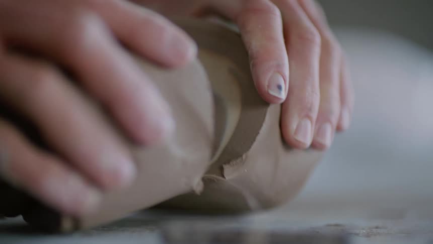 Human hands cutting a piece of clay in half using a tool