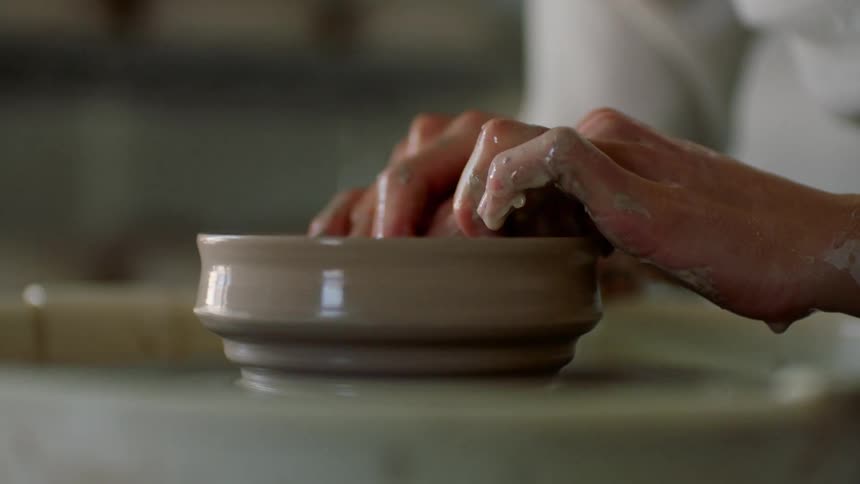 A woman shapes clay on a pottery wheel